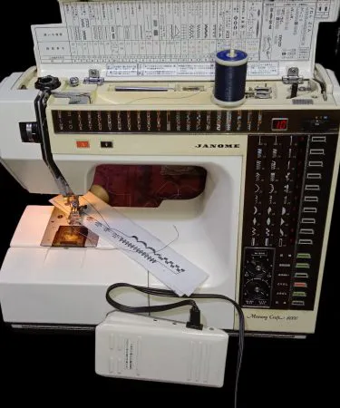 Janome Memory Craft 6000 (110V) computerized sewing machine with included voltage regulator, showing the control panel, free arm, and various accessories on a white background, available via Khareedo Pakistan