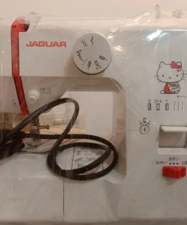 A vibrant red and white Jaguar Hello Kitty 110 Volt electric domestic sewing machine, featuring Hello Kitty branding on the front, visible stitch selector dial, red reverse lever, and start/stop buttons.