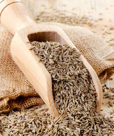 Close-up of golden-brown Premium Zeera (Cumin Seeds) in a wooden bowl, showcasing their pure, natural form and strong aroma, essential for authentic Pakistani cooking. Available for purchase on Khareedo with Check on Delivery and 100% satisfaction.