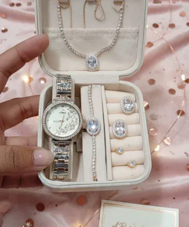 ** Hand in white glove holding open turquoise ladies jewellery box with gold watch, green gemstone necklace, and diamond earrings inside.