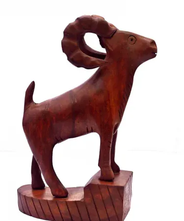 Hand‑carved wooden Markhor figurine with polished natural finish, displayed on a wooden tabletop.