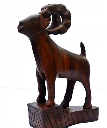 Hand‑carved wooden Markhor figurine with polished natural finish, displayed on a wooden tabletop.