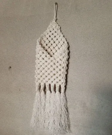 Hand‑made macrame mobile holder hanging on a wall, showcasing silk‑dori knots and a smartphone placed securely.