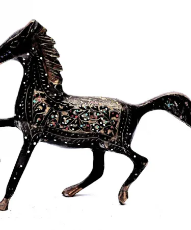 Handcrafted brass horse home decor with golden floral detailing on a wooden shelf, showcasing intricate engraved patterns and a stable base.