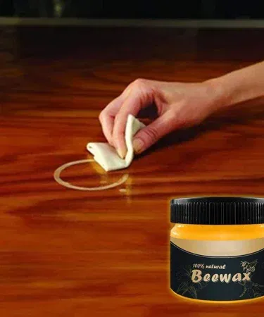 Natural beeswax polish in a white jar with a wooden brush, showing the creamy texture ready for application on wood and leather surfaces.
